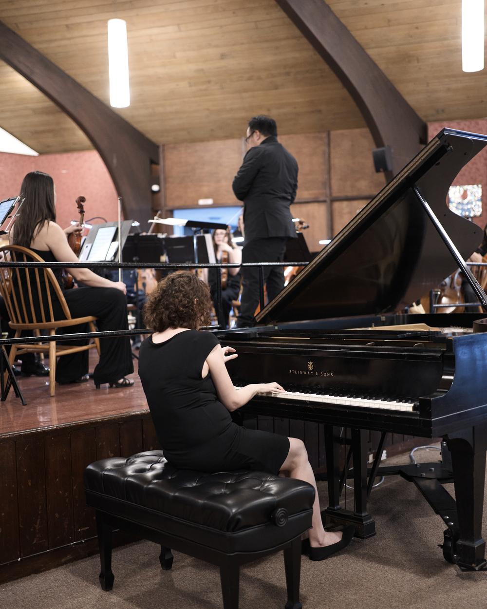 A pianist at the Steinway grand accompanying the orchestra from below the stage