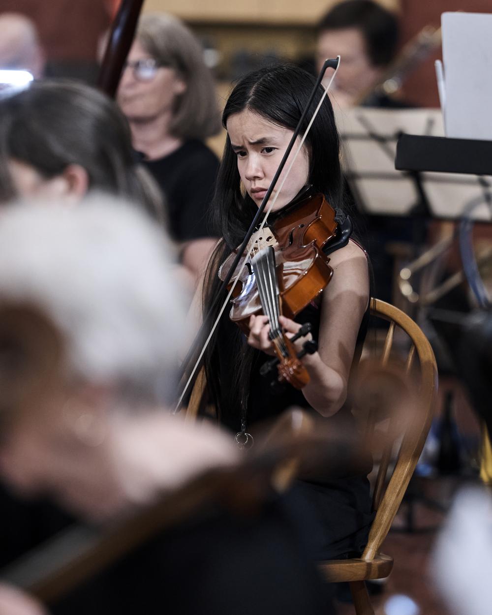 A young violinist playing in the middle of the string section during rehearsal